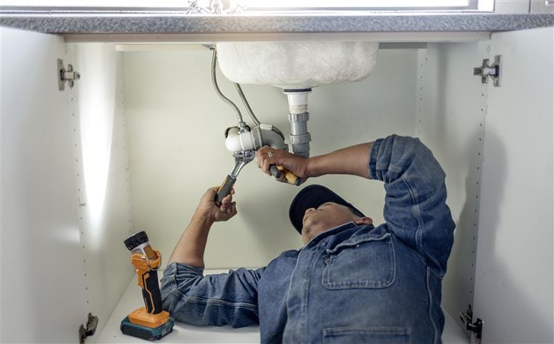 Plumber repairing pipes beneath a bathroom sink in Erie