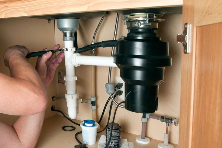 Plumber installing a garbage disposal beneath a kitchen sink in Erie