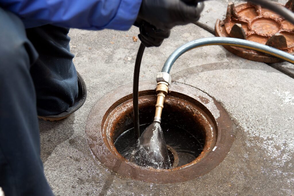 Plumber hydro jetting a sewer line through a manhole in Erie