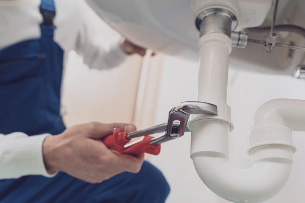 Plumber repairing a white drain pipe beneath a sink in Erie