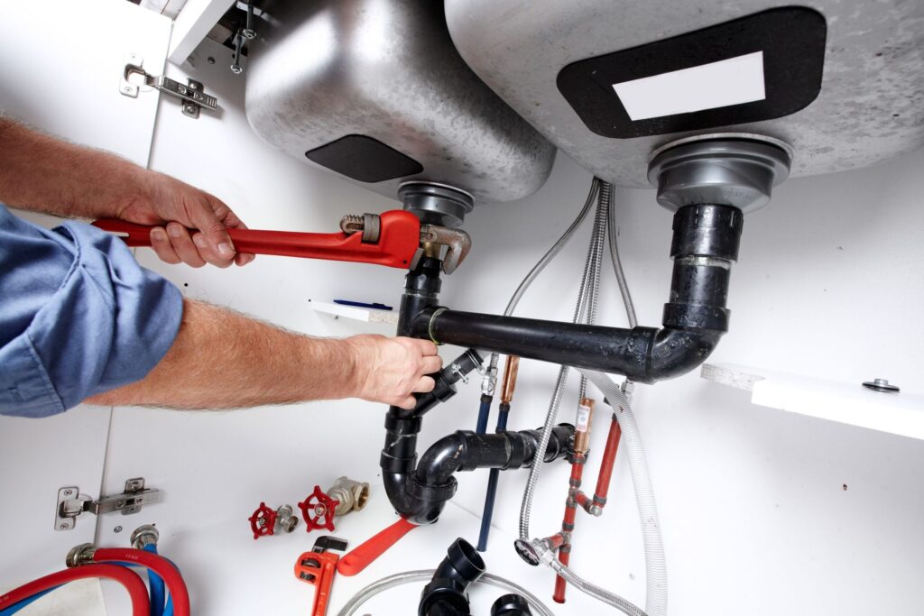 Plumber repairing drain pipes beneath a kitchen sink in Erie